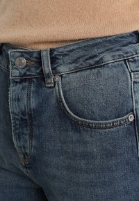 Denimjeans i medelblått med rak passform, klassisk femfickdesign och metalldetaljer vid midjan och fickorna.