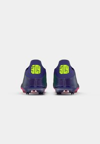 Botas con una parte superior morada texturizada, logo verde brillante y acentos rosas; diseñadas para el rendimiento con tacos para tracción.