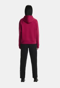 Bordová mikina s kapucňou a voľným strihom, s rebrovanými manžetami a lemom, v kombinácii s čiernymi nohavicami a športovou obuvou. Jednoduché pozadie.