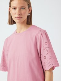 T-shirt en coton rose avec un design de broderie œillet sur les manches, présentant un col rond et des manches courtes et bouffantes. Texture lisse.