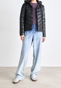 Czarna kurtka puchowa z kapturem i wzorem w jodełkę, zestawiona z jasnoniebieskimi szerokimi dżinsami oraz srebrnymi trampkami z białymi sznurowadłami.