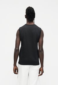 T-shirt preta de algodão sem mangas com decote redondo e corte descontraído, vista por trás, destacando a textura suave e o corte.