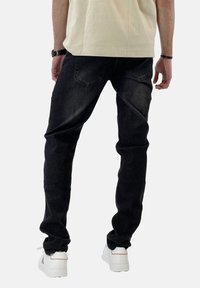 Vaqueros de mezclilla negros con un corte ajustado, que cuentan con bolsillos traseros y un ligero desgastado, combinados con zapatillas blancas.