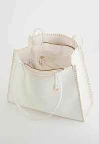 Sac à main en cuir blanc avec des coutures beiges, intérieur spacieux comprenant une poche zippée et deux poignées courtes. Surface texturée.