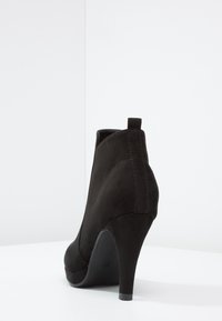 Černé semišové kotníkové boty s špičatou špičkou, vysokým podpatkem, hladkým povrchem a malým okem na zadní straně pro snadné obouvání.