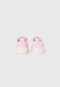 Une paire de baskets en daim rose clair avec des semelles blanches épaisses, vues de l'arrière sur un fond blanc uni.