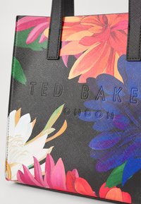 Črna torba z ročaji z rožnatimi cvetovi v živahnih odtenkih roza, oranžne in modre barve. Vključuje embosirano oznako "TED BAKER LONDON". Gladka textura, trdni ročaji.