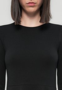 Black fitted long-sleeve top with a round neckline and smooth texture, featuring minimal seams and a simple, sleek design.