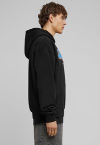 Zwarte hoodie van zachte stof, met een kangoeroezak en geribbelde manchetten. Versierd met kleurrijke grafische tekst aan de voorkant.