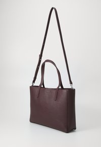 Sac fourre-tout en cuir bordeaux avec une finition texturée, des poignées doubles et une bandoulière réglable. Forme rectangulaire, design minimaliste.