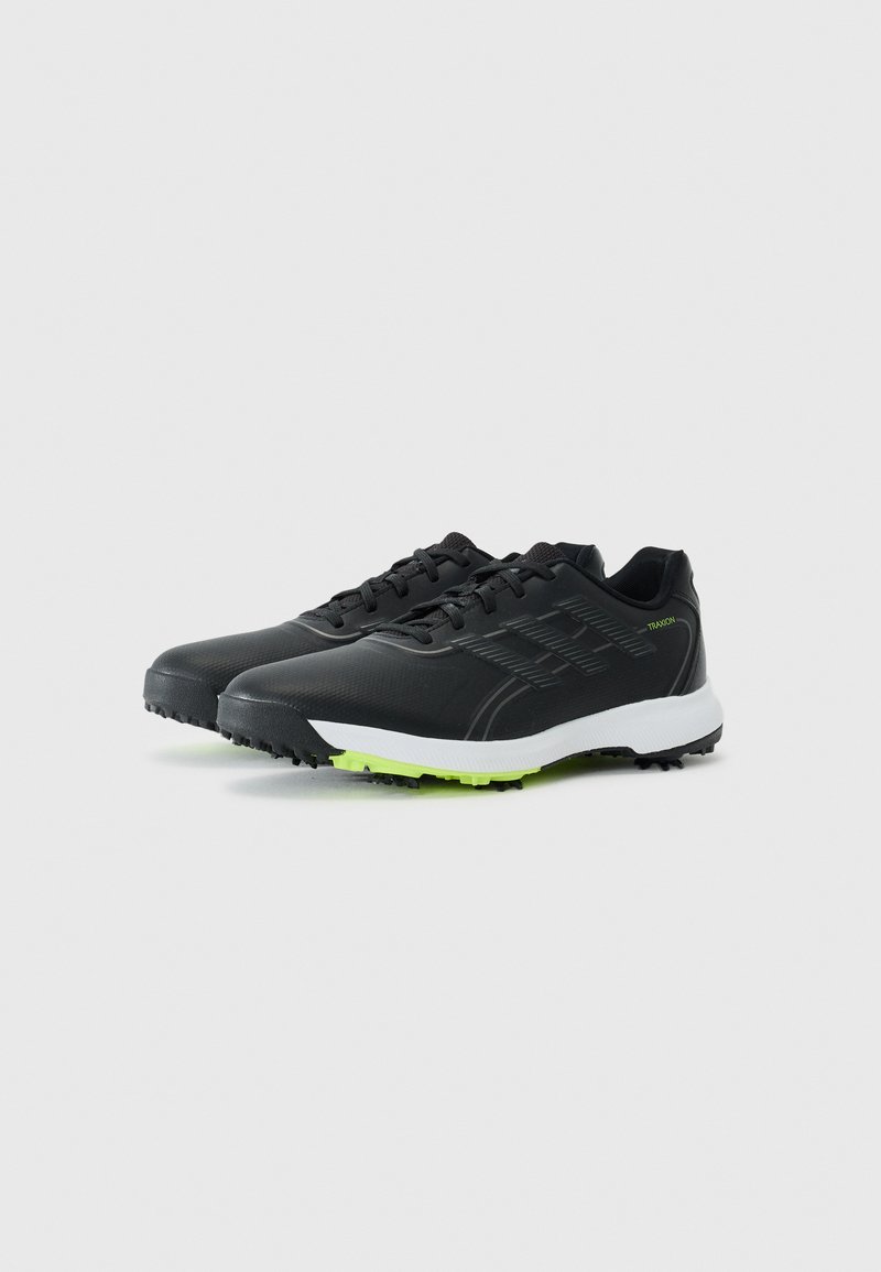 Schwarze Sportschuhe mit einer glatten Oberseite, strukturierten Akzenten, weißer Zwischensohle und grünen Außensohlenstollen für Traktion. Schnürdesign.