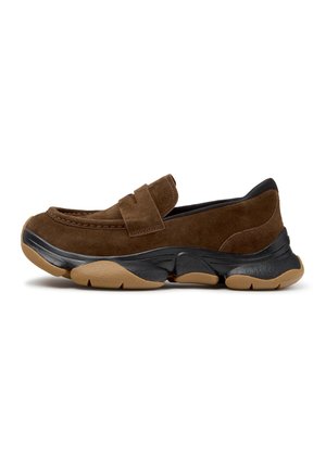 Brun ruskind slip-on sko med sort og tan chunky gummisål og en stropdetalje over toppen, vist fra siden.