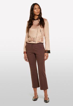 Veste de moto en suede beige avec une taille ceinturée, des poches zippées et un col structuré. Associée à un pantalon court marron et des ballerines noires.