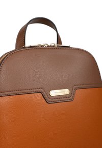 Bruine en oranje leren rugzak met een gestructureerde textuur, een ronde vorm, gouden hardware en een merkplaat aan de voorkant.