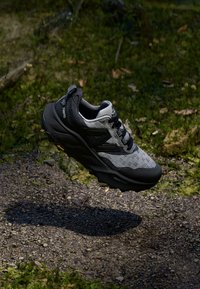 Chaussure de trail en noir et gris, avec une tige texturée, une semelle rembourrée et un logo bien en vue. Design léger avec une semelle extérieure robuste.