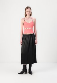 Korallkrāsu croptops ar regulējamiem siksniņām un metāliskām akcentiem, kombinēts ar melnu satīna midi svārku ar sānu izgriezumu un potītēm zābakiem.