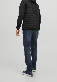 Black, quilted puffer jacket with a hood, paired with dark blue jeans and navy canvas sneakers. Simple design, no visible patterns.