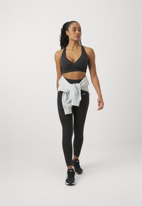 Svart sportsbh med v-halsdesign, kombinert med høy midje svarte leggings. En lys grå genser knyttet rundt livet. Svart treningssko.