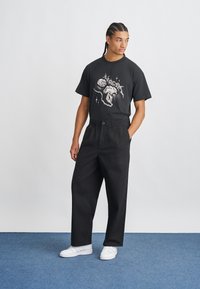 Svart bomull t-skjorte med grafisk design i hvitt. Kombinert med sorte, løse bukser og hvite joggesko. Enkel og minimalisk.