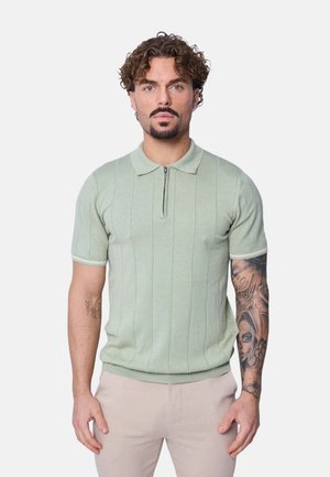 Polo en vert clair, texture côtelée avec une courte fermeture éclair, présentant des rayures subtiles et des accents blancs contrastés sur le col et les manches.