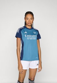 Blå och marinblå fotbollströja med texten "Emirates FLY BETTER", med vita ränder på axlarna och ventilerande material. Vita shorts och randiga strumpor.