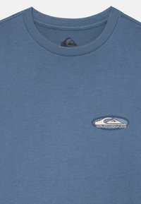 Mėlyna medvilninė T-maišeli su apvalia iškirpte ir siuvinėtu Quiksilver logotipu. Minkšta tekstūra, trumpomis rankovėmis, laisvalaikio dizainas.