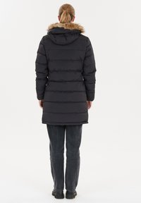 Puffet sort jakke med en hætte trimmet med pels, vertikal syning, knælængde design og båret med mørke jeans og solide sorte støvler.