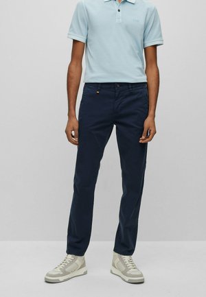 Polo shirt azzurro chiaro con maniche corte e colletto, abbinato a chinos blu scuro e sneakers alte beige.
