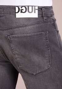 Gray denim jeans with a visible logo tag at the waistband. Features two rear pockets and classic stitching. Smooth texture.
