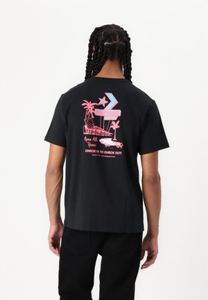 Tricou din bumbac negru cu un grafic pe spate, având palmieri, un semn de hotel și text în roz și albastru. Mâneci scurte, croială standard.