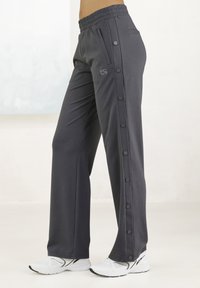 Gray athletic pants with a wide leg, featuring a drawstring waistband and snap button detailing along the sides. Paired with white sneakers.