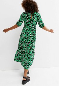 Vestido verde con estampado de leopardo, con mangas abullonadas, una espalda con abertura y una falda fluida. Lleva sandalias negras.