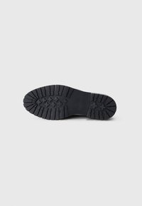 Black rubber shoe sole featuring a grooved pattern for traction, with raised accents in the shape of crosses and ridges.