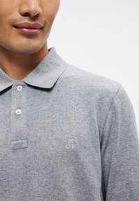 Polo grigio con colletto, due bottoni e logo ricamato "MOP". Tessuto morbido con una texture sottile.