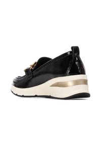 Zapatos de charol negros con un diseño elegante, que presentan un detalle dorado y una gruesa suela blanca con una franja dorada en el talón.