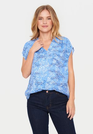 Blue short-sleeve top with a V-neck, featuring a textured pattern in light and dark blue hues. Paired with dark denim jeans.