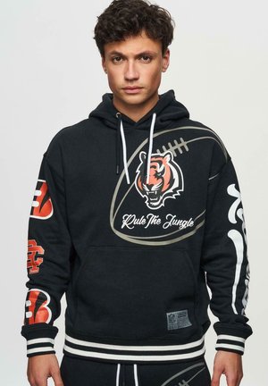 Zwart hoodie met een tijgerafbeelding, "Heers over de Jungle" tekst, NFL-branding en gedurfde rode accenten op de mouwen. Gestreepte boorden en zoom.