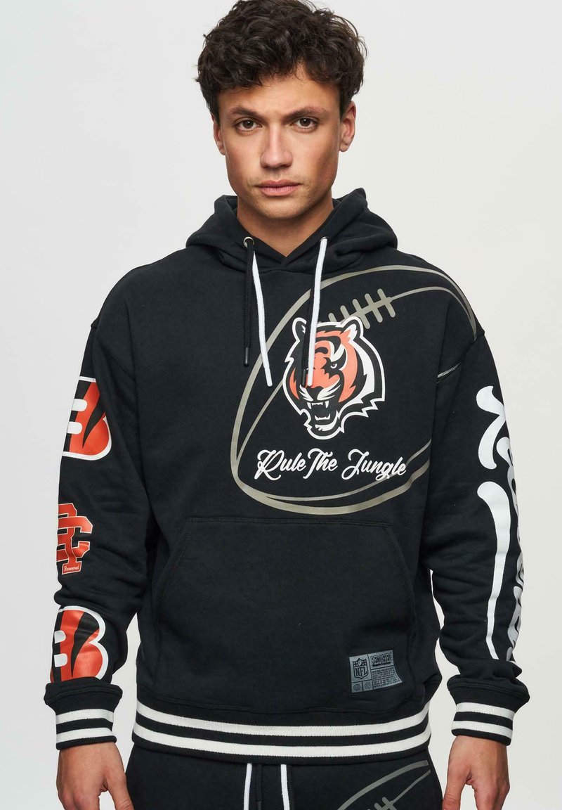 Felpa nera con cappuccio caratterizzata da una grafica di una tigre, testo "Regna sulla Giungla", marchio NFL e audaci accenti rossi sulle maniche. Polsini e orlo a righe.