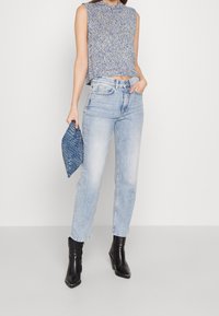 Niebieski dzianinowy top bez rękawów, jasnoniebieskie jeansy z wysokim stanem, czarne botki za kostkę oraz teksturowana niebieska kopertówka z motywem węża.