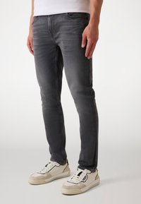 Vaqueros de mezclilla gris ajustados con un acabado desgastado, diseño de cinco bolsillos y cremallera. Combinados con zapatillas bajas blancas y beige.