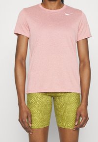 Camiseta atlética de mangas cortas en rosa claro con cuello redondo y un logo blanco en el pecho, combinada con pantalones cortos de ciclismo verdes con estampado.