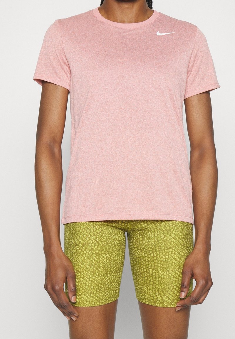 Camiseta atlética de mangas cortas en rosa claro con cuello redondo y un logo blanco en el pecho, combinada con pantalones cortos de ciclismo verdes con estampado.