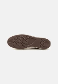 Semelle en caoutchouc marron d'une basket avec motifs géométriques sur la bande de roulement et marquage "All Star" au centre sur fond blanc.