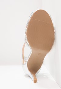 Sandale à talon argentée au design épuré, avec un bout pointu, des fines brides à la cheville et une semelle texturée pour une meilleure adhérence.