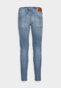 Vaqueros ajustados de un azul claro, fabricados en denim; cuentan con dos bolsillos traseros con detalles de costura y una etiqueta de cuero marrón en la cintura.