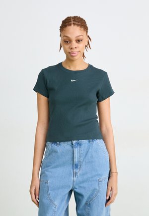 Mørkegrøn ribbet crop t-shirt med korte ærmer og rund halsudskæring, med et lille hvidt Nike-logo på brystet. Bæret sammen med lyseblå denimjeans.