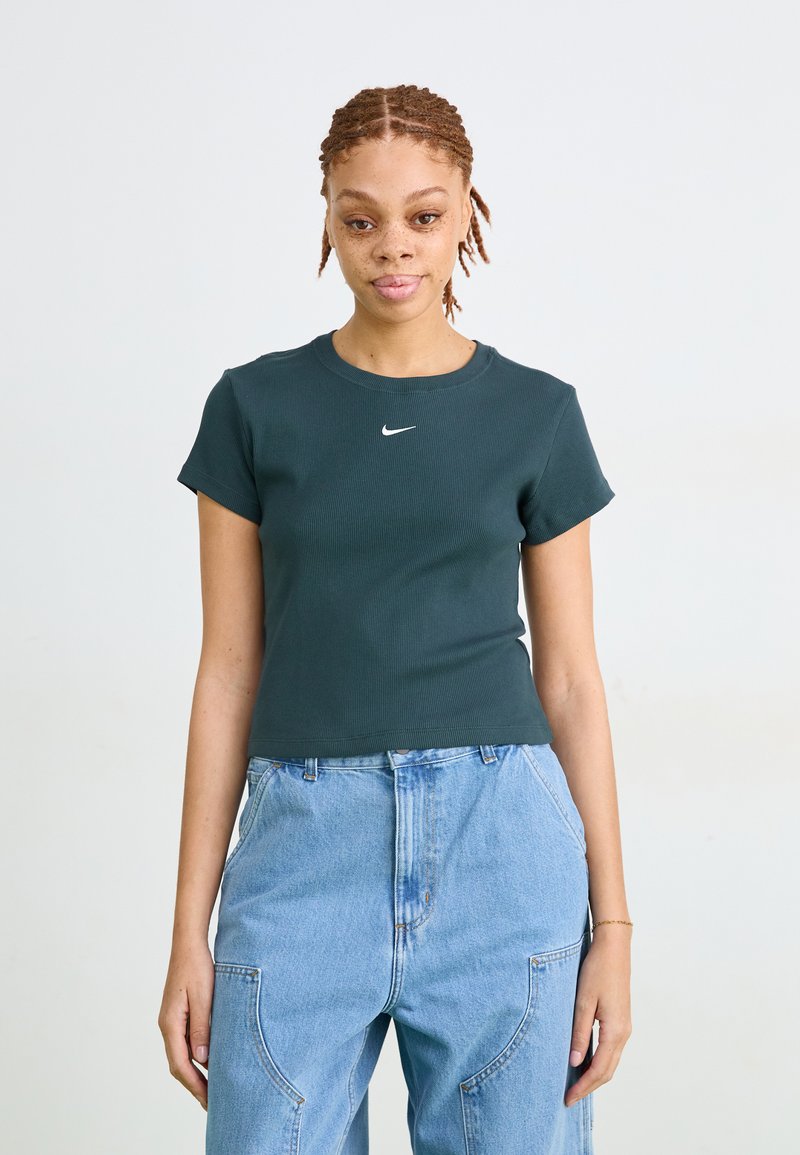 Tamsiai žalia juostuota trumpa marškinėlių su trumpomis rankovėmis ir apvali iškirpte, ant krūtinės yra mažas baltas Nike logotipas. Dėvimi su šviesiai mėlynomis džinsinėmis kelnėmis.
