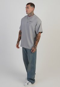 Hall hall, lühikeste varrukatega T-särk, millel on lõdvestatud istuvus ja rinnal logo. Kombineeritud ühelt poolt lõdva sinise teksapüksi ja valgete tossudega.