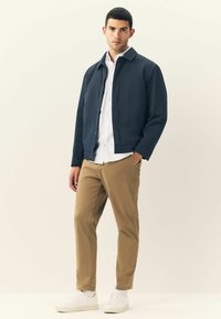 Giacca navy con colletto, camicia bianca con bottoni, pantaloni khaki e sneakers bianche. Design semplice con una texture liscia e vestibilità dritta.