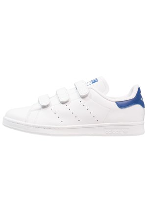 Baskets basses blanches avec trois bandes Velcro, détails perforés sur les côtés et languette de talon bleue avec logo.